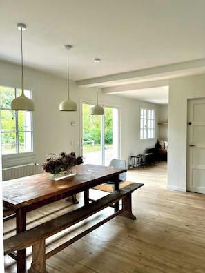 A spacious room with a wooden dining table, hanging pendant lights, and large windows offering a view of greenery outside. - Charming house in Lyons-la-Forêt (Lyons-la-Forêt)