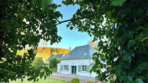 Ein Haus mit schrägem Dach, umgeben von einem Rasen und Bäumen.