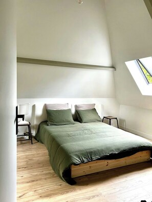 A bedroom with a sloped ceiling, a skylight, a bed with green bedding, a chair, and a small table. - Charming house in Lyons-la-Forêt (Lyons-la-Forêt)