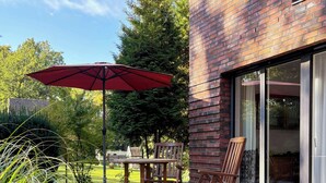 An outdoor patio with a table and chairs, a red umbrella, and a brick wall. - House with private jetty on Neversdorfer See (Leezen)