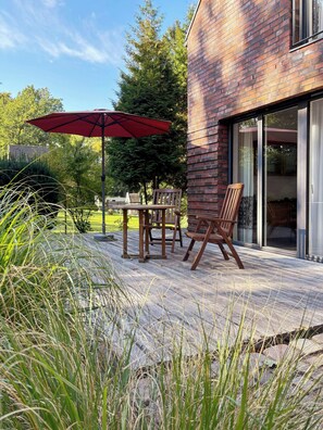 An outdoor patio with a table and chairs, a red umbrella, and a brick wall. - House with private jetty on Neversdorfer See (Leezen)