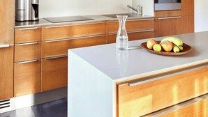 A modern kitchen with wooden cabinets, stainless steel appliances, and a central island with a bowl of fruit. - House with private jetty on Neversdorfer See (Leezen)
