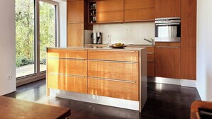A modern kitchen with wooden cabinetry, a stainless steel oven, and a large window. - House with private jetty on Neversdorfer See (Leezen)