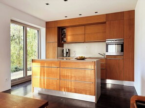 A modern kitchen with wooden cabinetry, a stainless steel oven, and a large window. - House with private jetty on Neversdorfer See (Leezen)