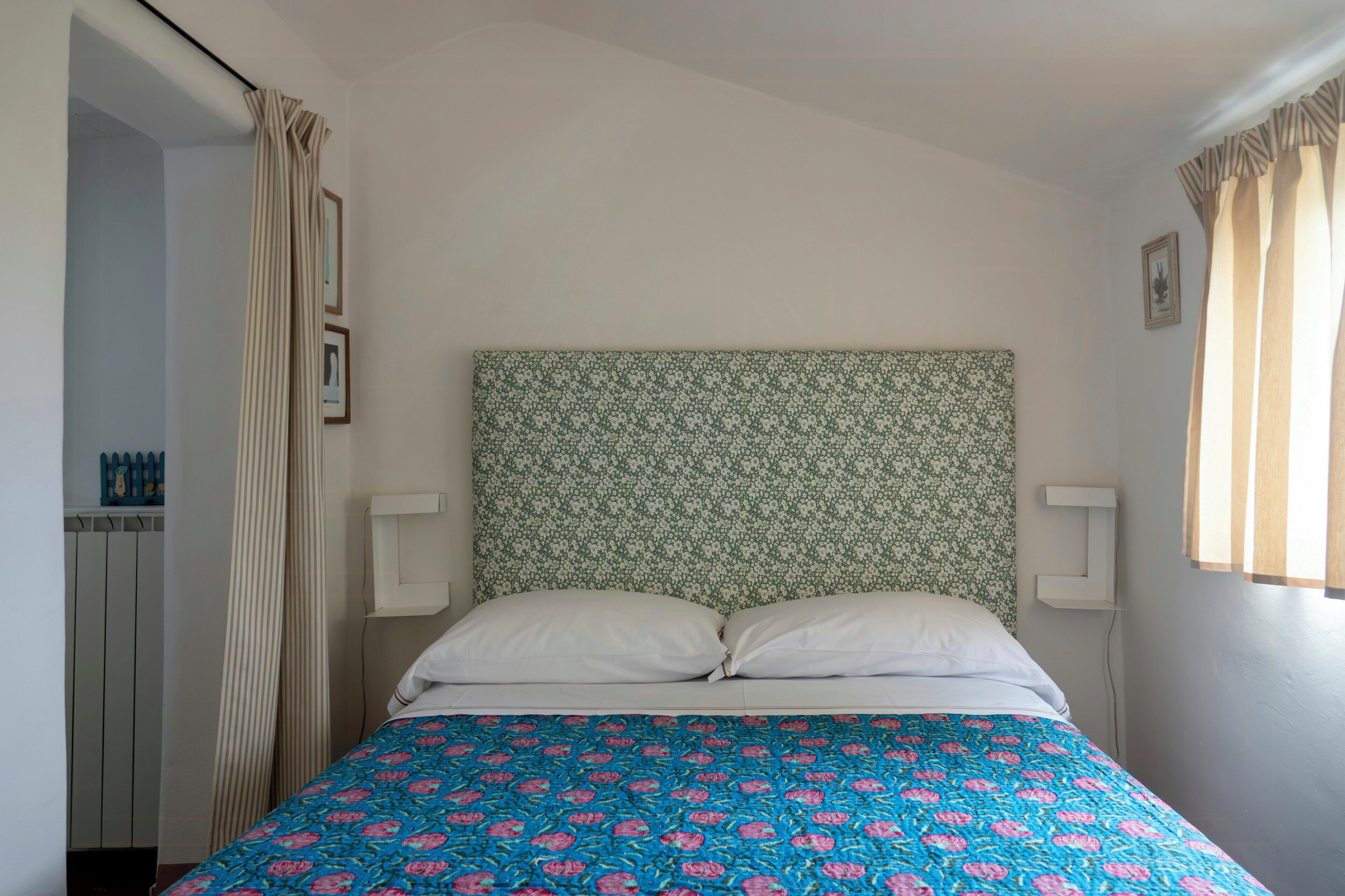 A bed with a patterned headboard, a white pillow, and a blue floral bedspread.