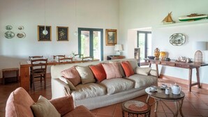 A living room with a sofa, chairs, a dining table, and a kitchen area with a shelf. - Traditional Tuscan villa on hill with pool (Magliano in Toscana)