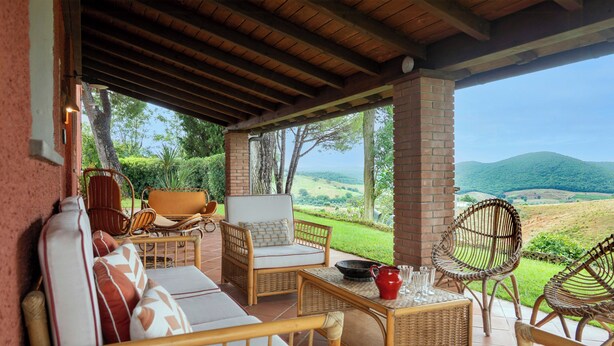 A covered patio with wicker furniture, a brick pillar, and a view of the countryside. - Traditional Tuscan villa on hill with pool (Magliano in Toscana)