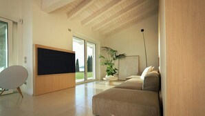 Ein modernes Wohnzimmer mit Flachbildfernseher, einer Couch, einer Topfpflanze und einem großen Fenster.