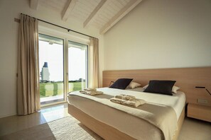 A modern bedroom with a large bed, a nightstand, and a view through the glass door. - Villa with infinity pool overlooking Lake Garda (Bardolino)