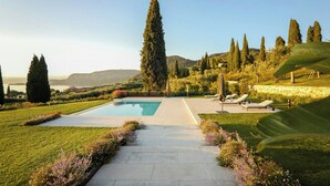 Ein Pool mit einem gepflasterten Weg zu Liegestühlen, umgeben von gepflegten Rasenflächen und hohen Bäumen.