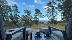 Eine Terrasse mit zwei Stühlen und einem Tisch, mit Blick auf einen Wald und eine ferne Aussicht.