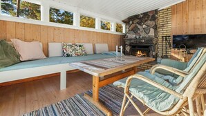 Una sala de estar acogedora con chimenea de piedra, paneles de madera, un banco acolchado, sillas de mimbre y un televisor.