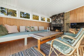 Ein gemütliches Wohnzimmer mit Kamin aus Stein, Holzwandverkleidung, einer gepolsterten Bank, Korbstühlen und einem Fernseher.