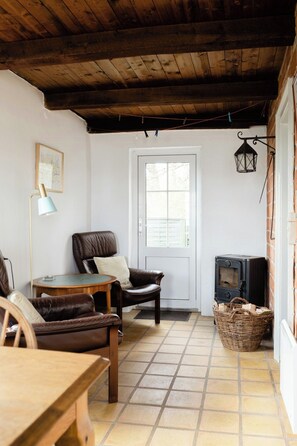 Ein gemütliches Zimmer mit Holzboden, Kamin, Tür, Stuhl, Tisch und Lampe.