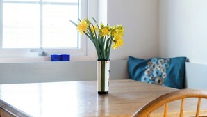 Ett matbord med stolar, en hängande taklampa, en vas med blommor och ett fönster med blå gardiner.