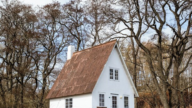 Ett vitt hus med ett brunt tak, omgivet av träd.