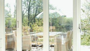 Quarto com janelas amplas, móveis de vime e vista para um jardim e árvores.