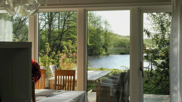 Quarto com cama, mesa e cadeira, vista para um lago e floresta.