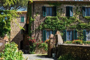 Ein Steinhaus mit grünen Fensterläden, einer Steintreppe und einem Garten mit roten Blumen.