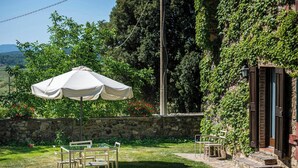 Un muro in pietra, posti a sedere all'aperto e un ombrellone bianco in un giardino.
