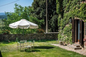 Eine Steinsäule, Sitzgelegenheiten im Freien und ein weißer Sonnenschirm in einem Garten.