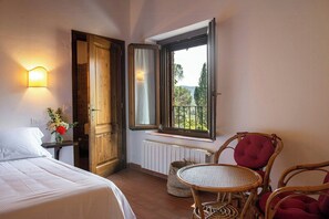 Ein Hotelzimmer mit einem Bett, einem kleinen Tisch, Korbstühlen, einem Fenster mit Blick und einer Wandleuchte.