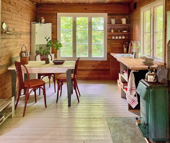 A wooden cabin interior with a dining table, chairs, a sink, and a stove. - Off-grid cabin in your private Swedish forest (Simlångsdalen)
