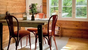 A wooden-paneled room with a dining table, chairs, a vase with flowers, and a window with a view of greenery. - Off-grid cabin in your private Swedish forest (Simlångsdalen)