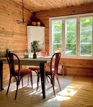 A wooden-paneled room with a dining table, chairs, a vase with flowers, and a window with a view of greenery. - Off-grid cabin in your private Swedish forest (Simlångsdalen)