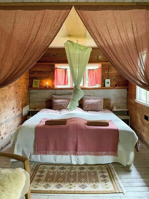 A cozy bedroom with a bed, pillows, a canopy, and a window with curtains. - Off-grid cabin in your private Swedish forest (Simlångsdalen)