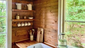 A wooden cabin kitchen with a window, wooden shelves, a sink, and a metal pitcher. - Off-grid cabin in your private Swedish forest (Simlångsdalen)