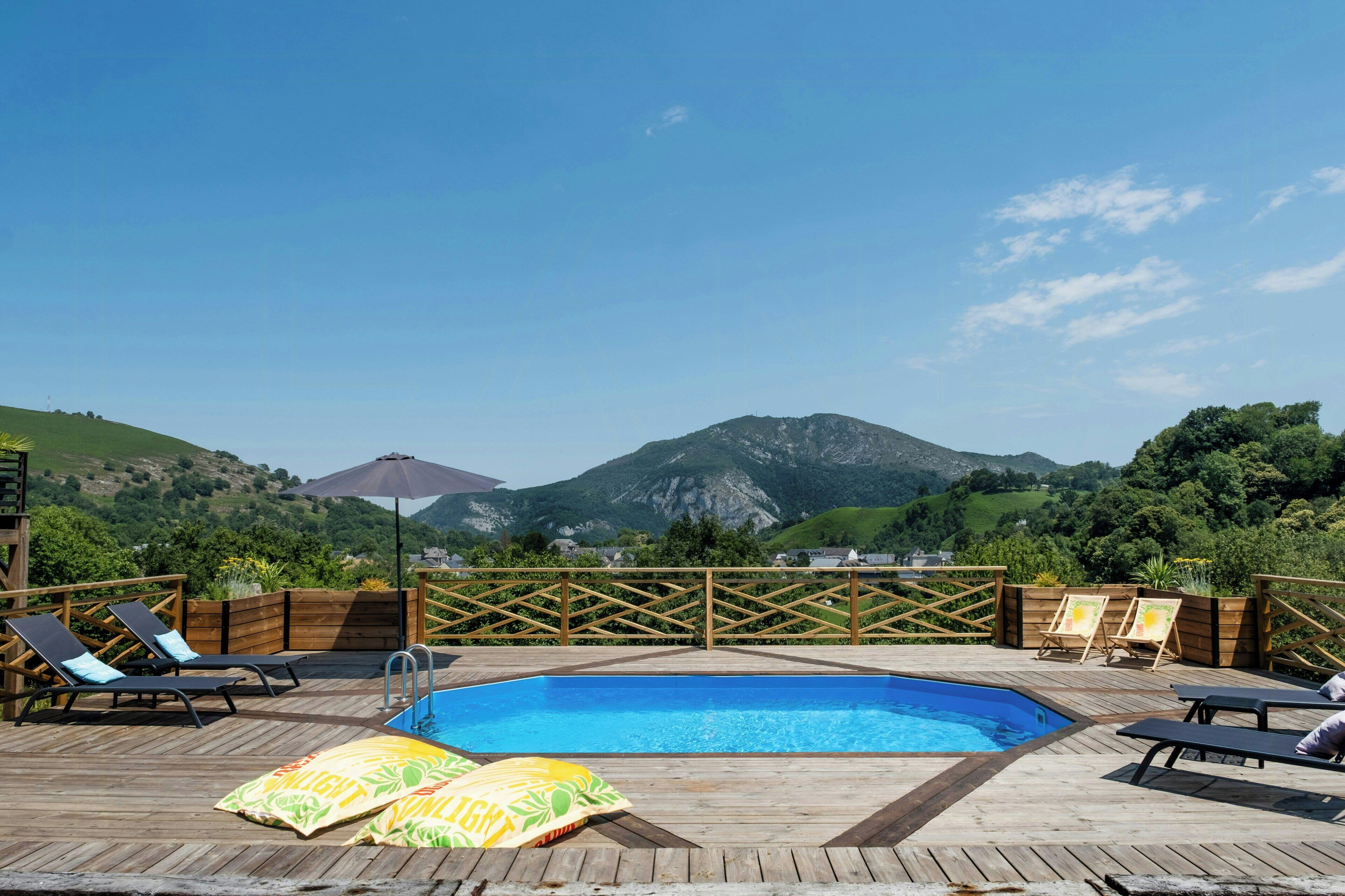A wooden deck with a pool, lounge chairs, and a view of mountains.