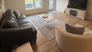 Una sala de estar moderna con sofá, sillón, televisor y vistas al balcón.