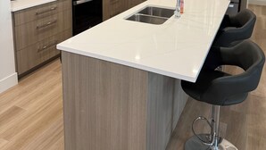Una cocina moderna con armarios de madera, electrodomésticos de acero inoxidable, una isla central con un lavamanos y taburetes negros.