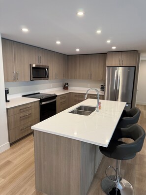 Eine moderne Küche mit Holzschränken, Edelstahlgeräten, einer zentralen Kochinsel mit Spüle und schwarzen Barhocker.