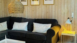 A modern living room with a black sofa, a white coffee table, a woven pendant light, framed pictures on the wall, and a small side table with a lamp. - Holiday home by Ålbæk Beach for the whole family (Ålbæk)