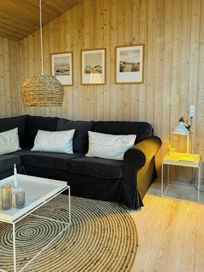 Ein modernes Wohnzimmer mit einem schwarzen Sofa, einem weißen Couchtisch, einer gewobenen Pendelleuchte, gerahmten Bildern an der Wand und einem kleinen Beistelltisch mit einer Lampe.