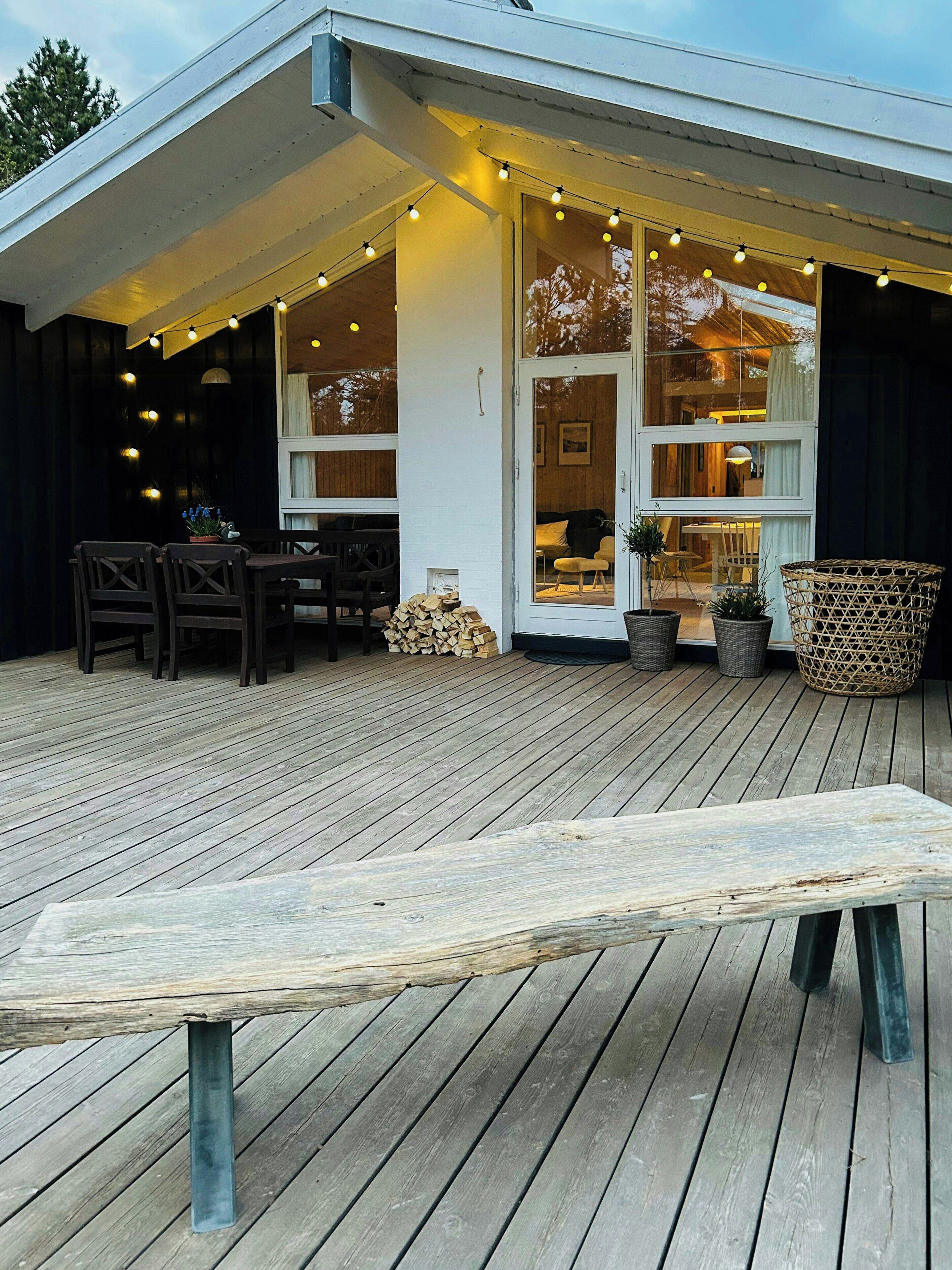 A wooden deck with a bench, chairs, and a table. There are string lights and potted plants.