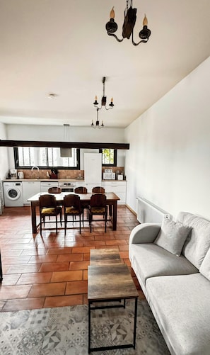 Eine moderne Küche mit weißen Schränken, ein Essbereich mit Tisch und Stühlen, ein graues Sofa und ein gemustertes Teppich.