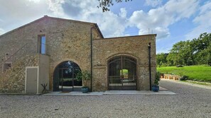 Ein Steinhaus mit großem Bogenportal, einem kleinen Balkon und einer Schotterzufahrt.