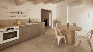 A modern kitchen with a built-in oven, a dining area with a round table and white chairs, and a hallway leading to another room. - Tuscan apartment with panoramic terrace (Montescudaio)