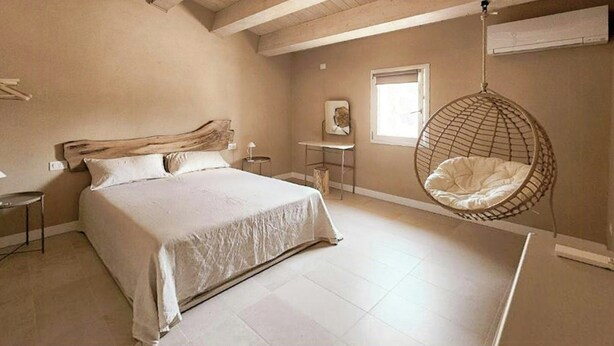 A bedroom with a large bed, a hanging chair, a small table, and a window. - Tuscan apartment with panoramic terrace (Montescudaio)