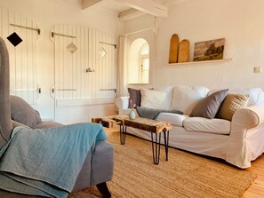 Ein Zimmer mit einem weißen Sofa, einem blauen Sessel, einem Holztisch und einem rustikalen Teppich.