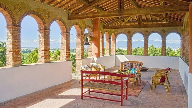 Une terrasse dotée d’un plafond en bois, d’arcs en briques, de meubles en osier et d’une table sur laquelle sont disposés divers objets.