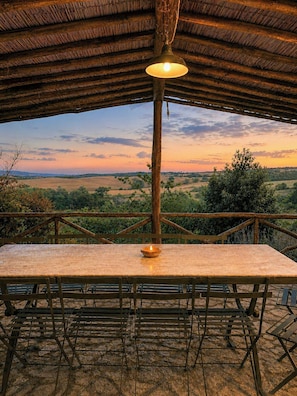 Ein Essbereich im Freien mit Tisch und Stühlen, einer hängenden Leuchte und Blick auf die Landschaft bei Sonnenuntergang.