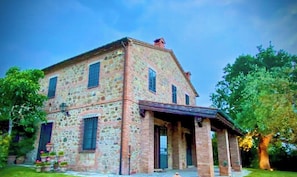 Ein Steinhaus mit Veranda, zahlreichen Fenstern und einem Ziegelkamin.
