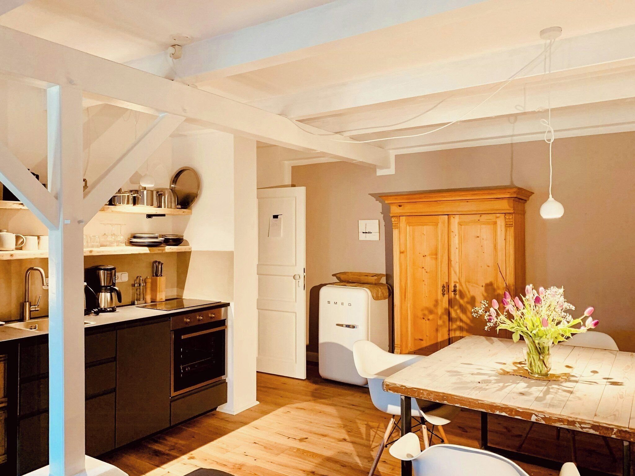 Een keuken met een houten tafel, witte stoelen, een koelkast en een houten kast.