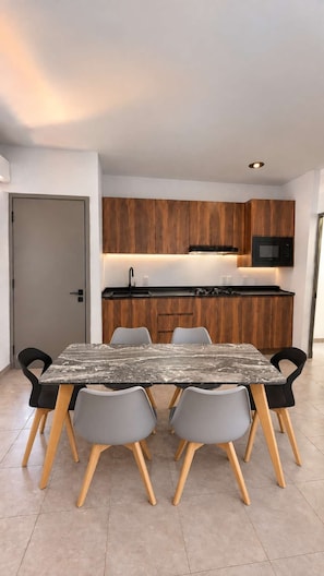 A modern kitchen with wooden cabinets, a black microwave, and a marble-top dining table with four chairs. - Departamento privado, Milan Providencia (Guadalajara)