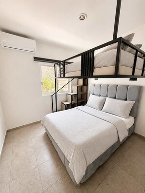 Een slaapkamer met stapelbed, raam, ingebouwde planken en een plafondventilator.