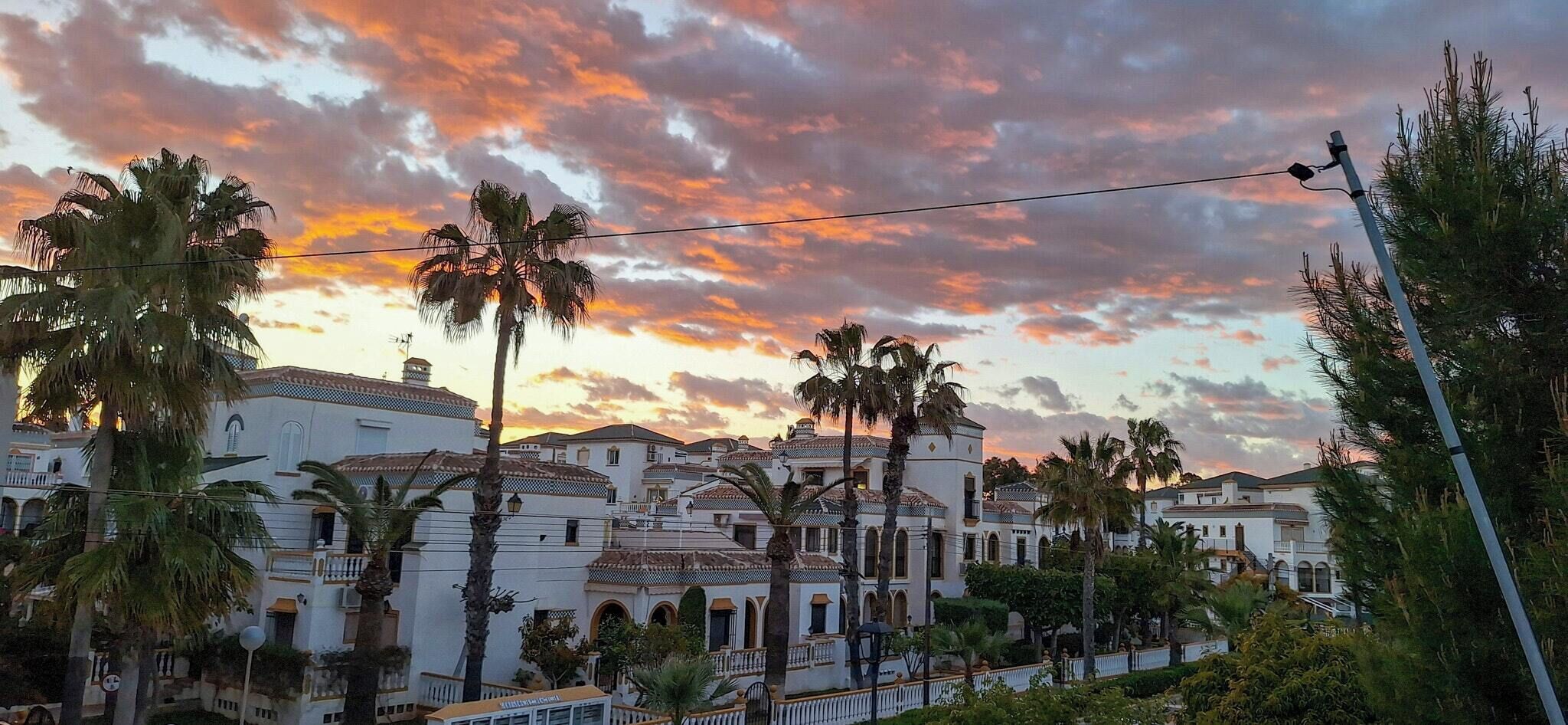 Eine Küstenstadt mit weißen Gebäuden, Palmen und einem Sonnenuntergangshimmel.